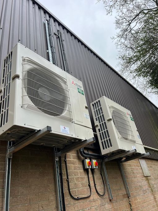 Two white Mitsubishi air conditioning units mounted on the exterior of a building with a corrugated metal wall.