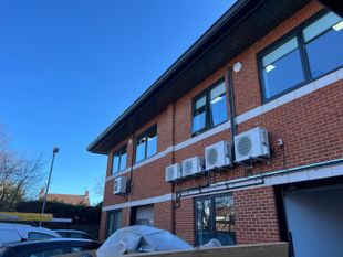 Red brick building with air conditioning units and black pipes against a clear blue sky.