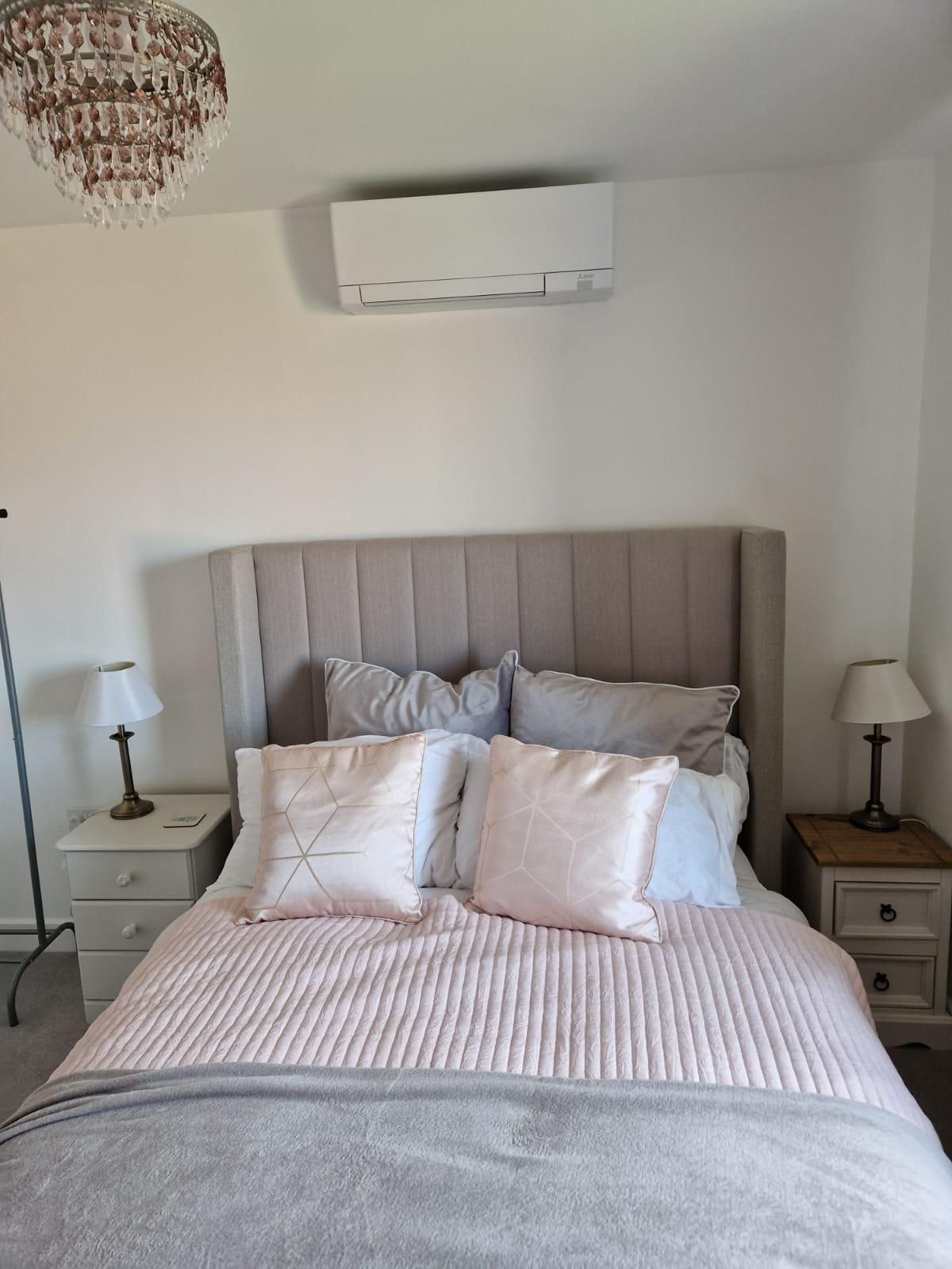 Bedroom with a gray upholstered bed, light pink bedding, and an air conditioning unit above the headboard.