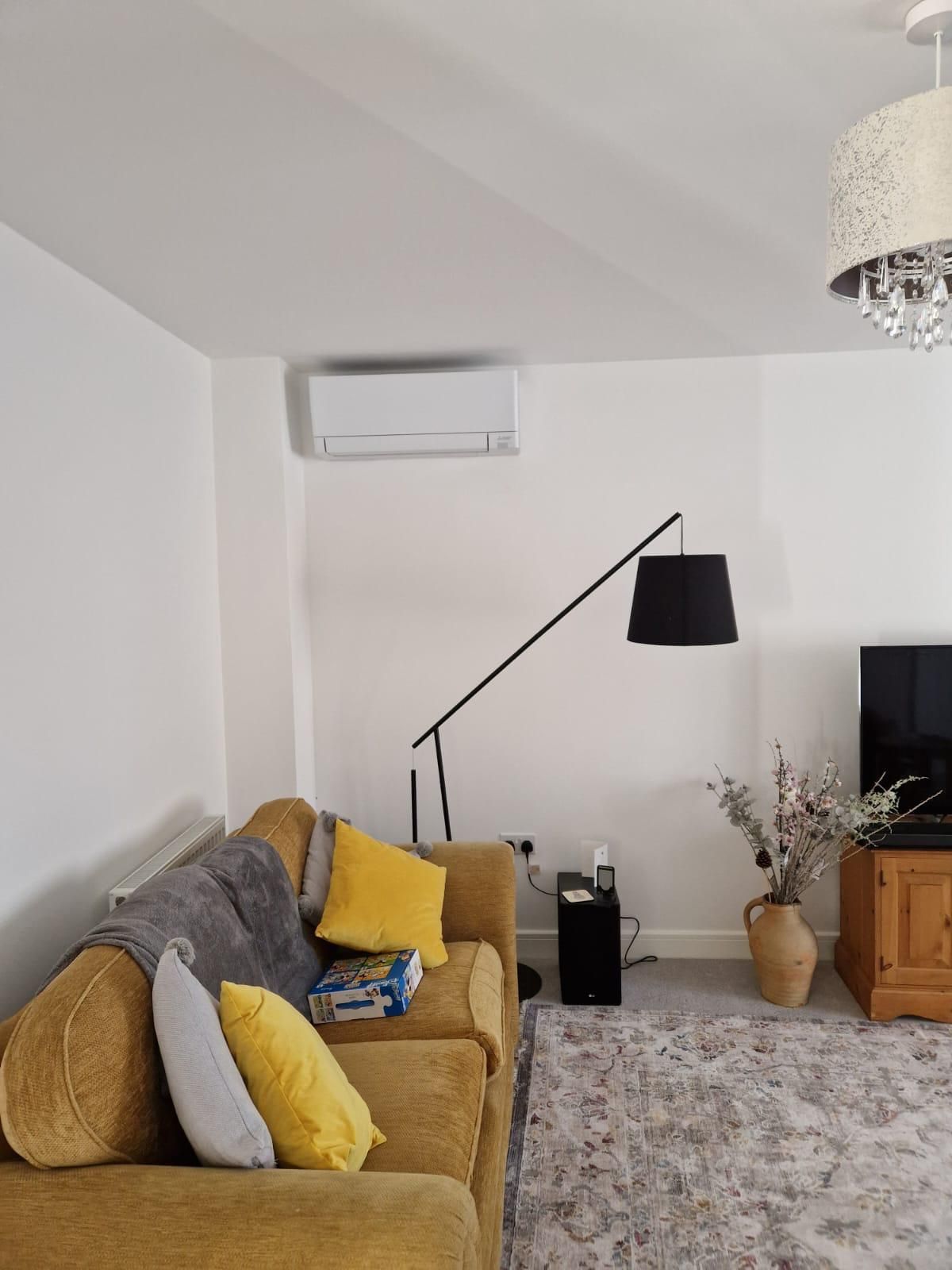 Living room with mustard sofa, white walls, AC unit, black lamp, rug, and TV stand.