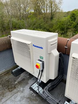 Panasonic outdoor AC unit on a rooftop, with electrical components and surrounding greenery.