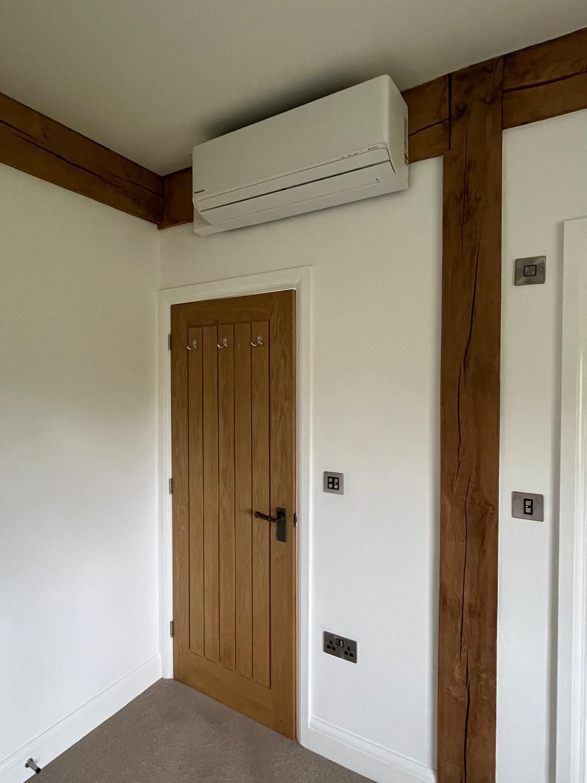 White air conditioning unit above a wooden door and outlet on a white wall.