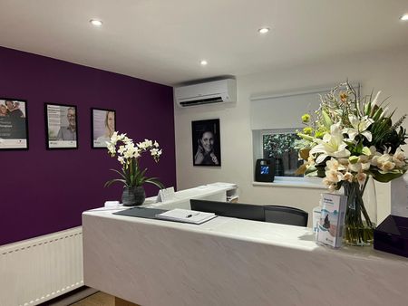 Reception desk with purple accent wall, art, and floral arrangements.