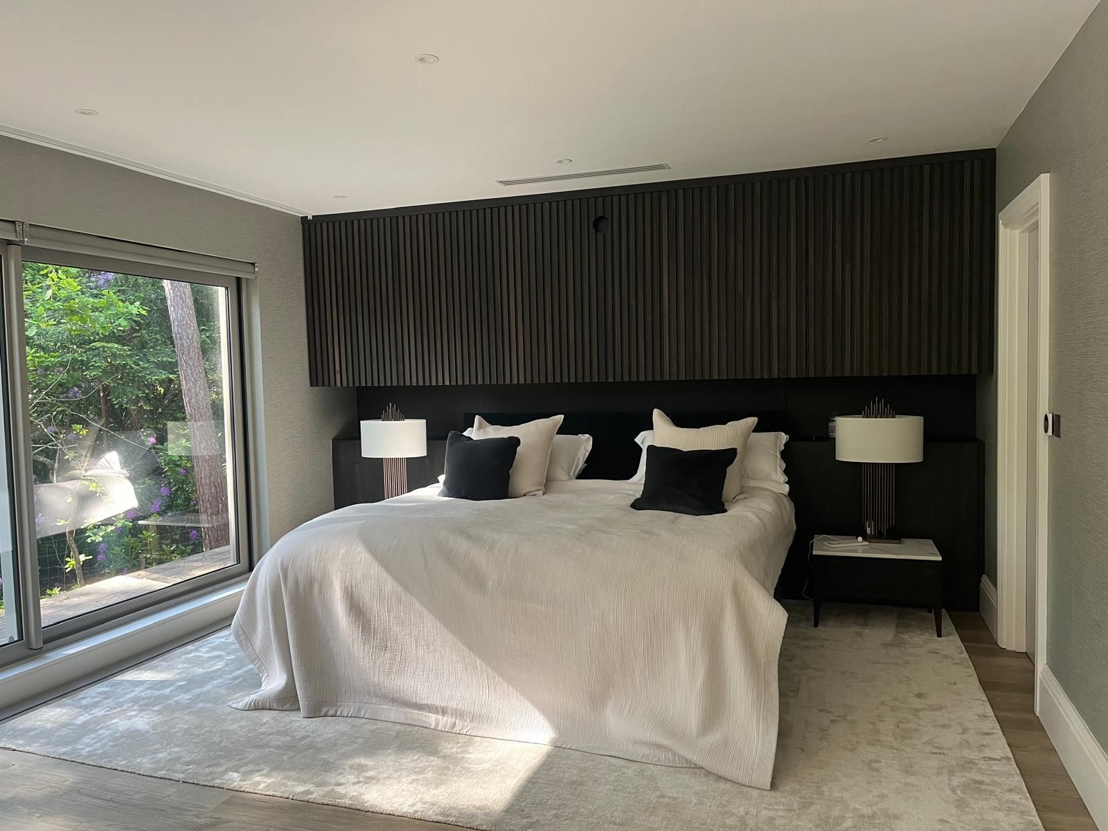 Bedroom with king-size bed, textured black headboard, two lamps, and large window.