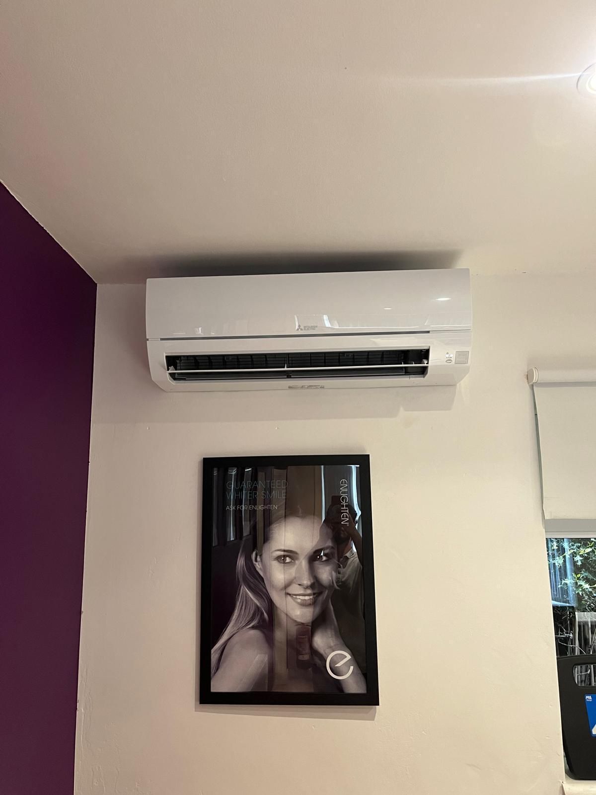 White air conditioner unit mounted above a framed black and white portrait on a white wall.