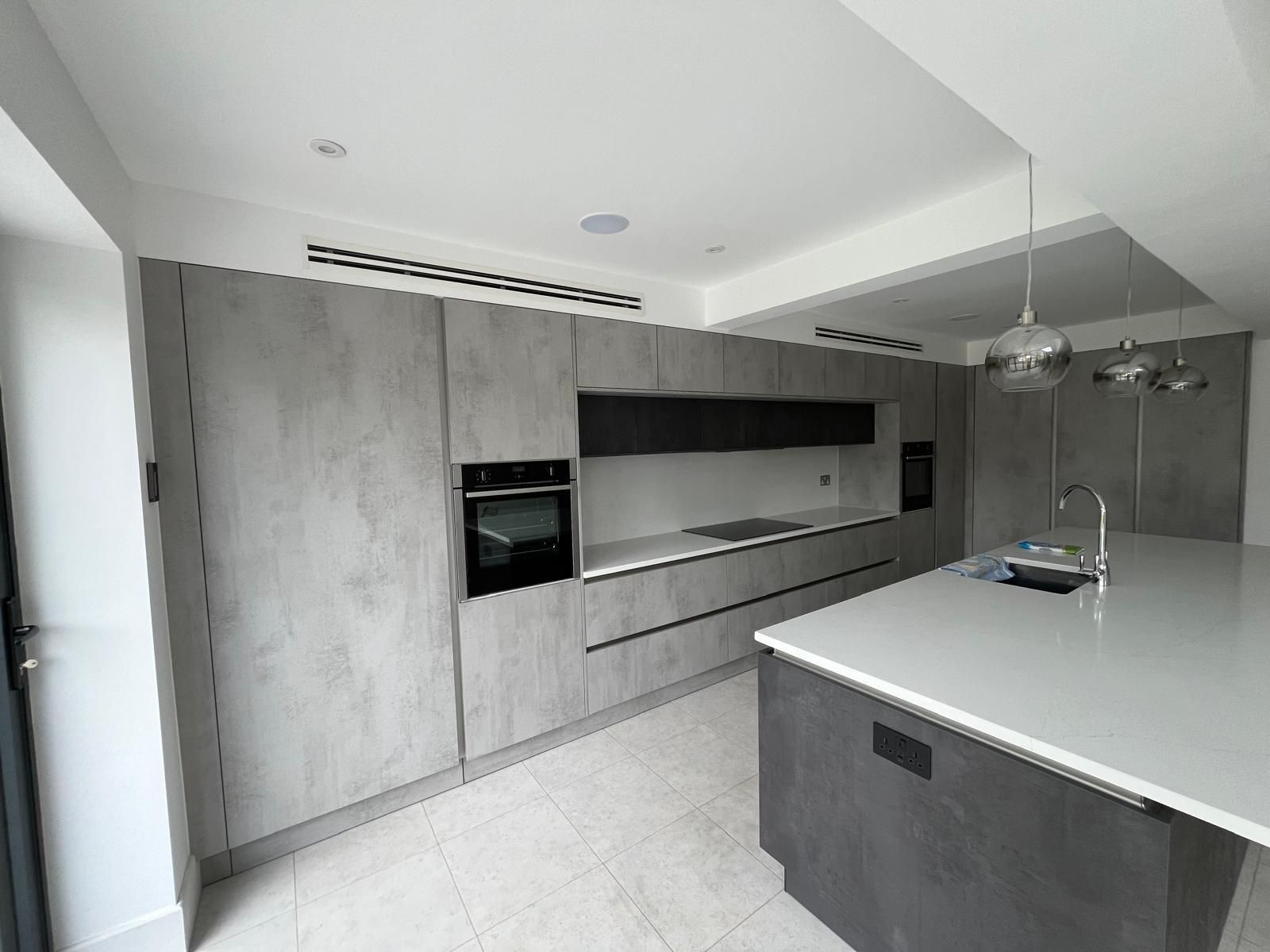 Modern gray kitchen with built-in appliances, white countertop island, and pendant lights.