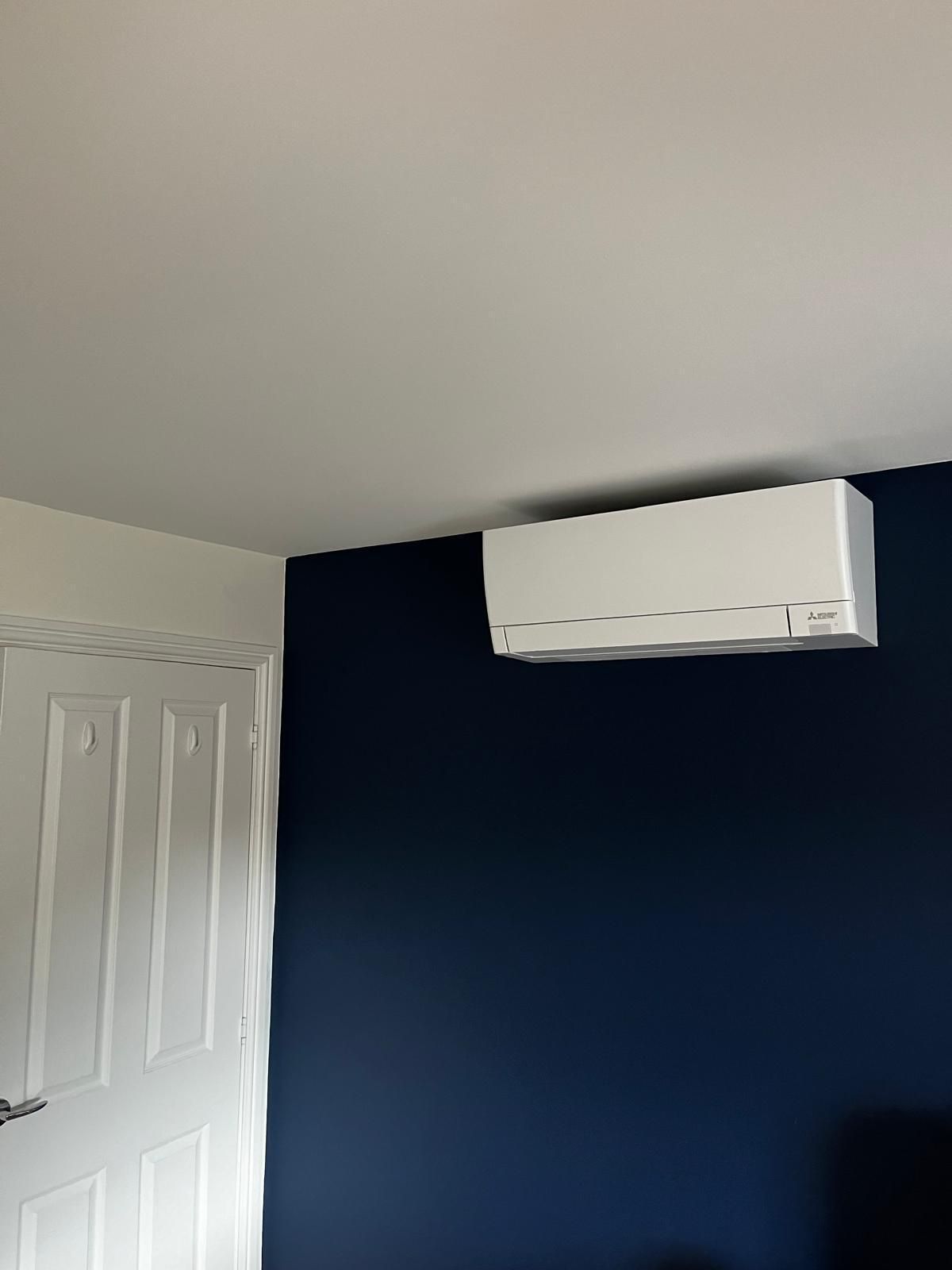 White wall-mounted air conditioner on a dark blue wall. A white door is on the left.