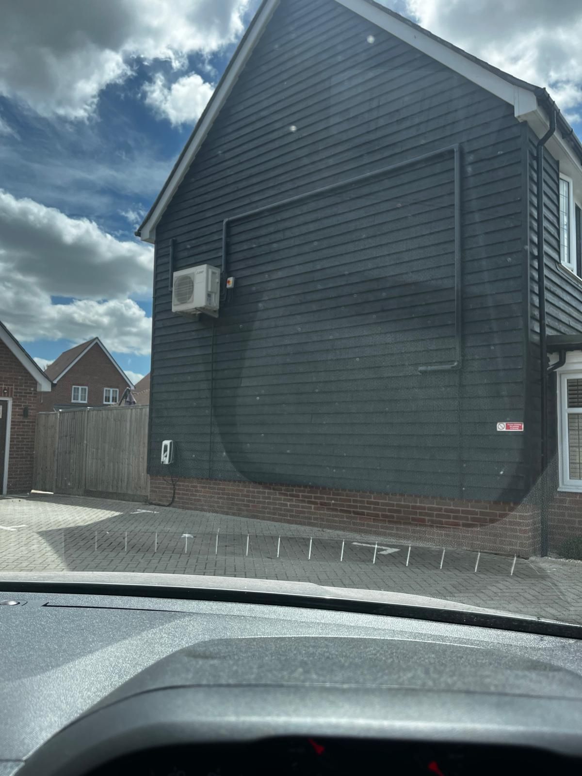 Dark gray house with air conditioner unit. Cloudy sky overhead.