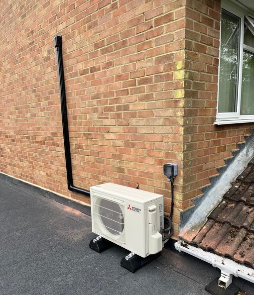 An air conditioning unit sits on black blocks next to a brick building.