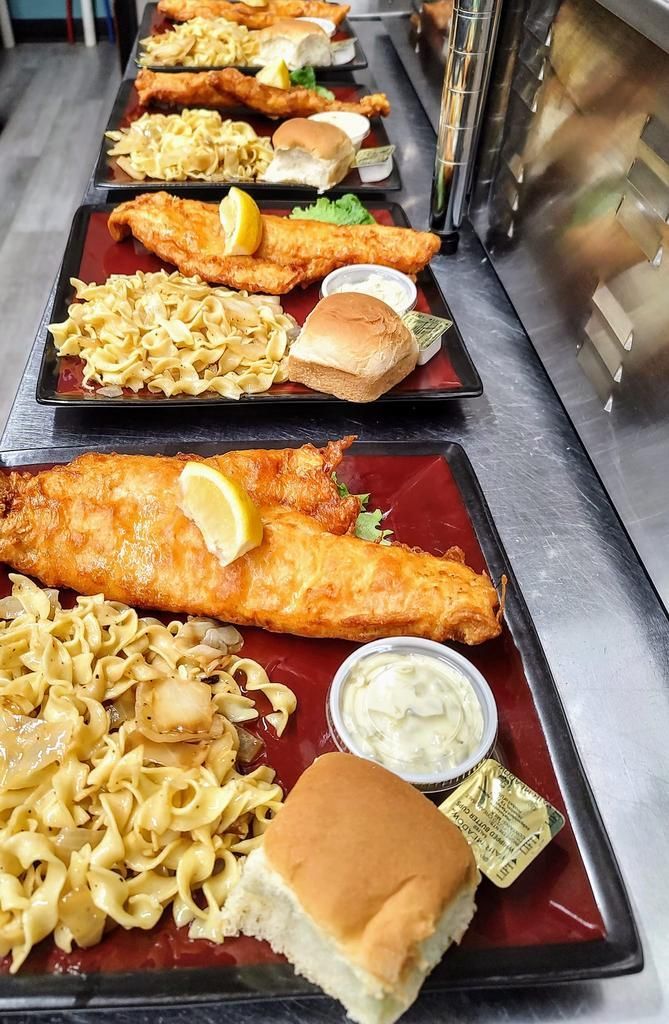 several plates of food including fish and noodles are lined up on a counter