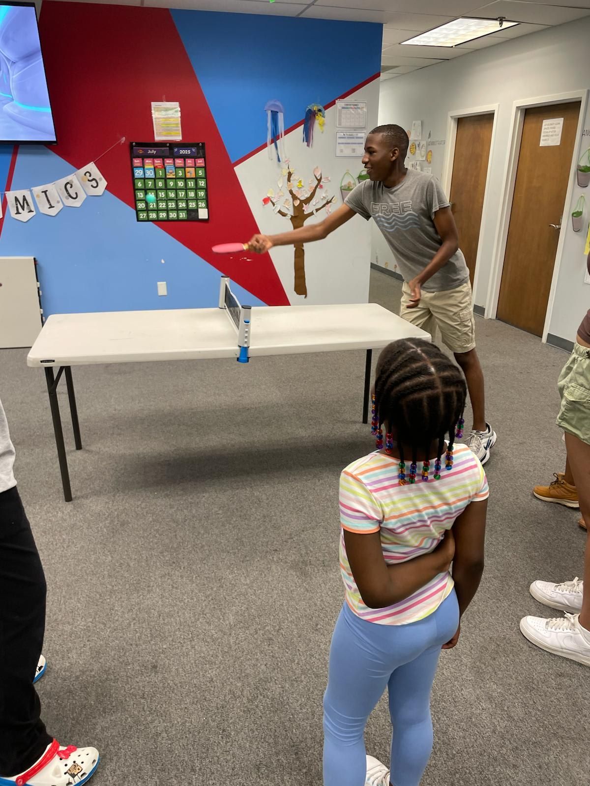 Man playing ping pong with children in a room with blue and red walls.