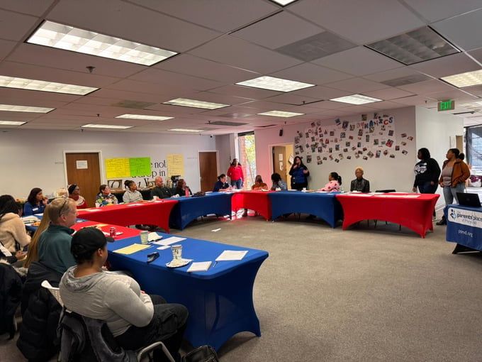Meeting in a room, people seated around a U-shaped table covered in red and blue.