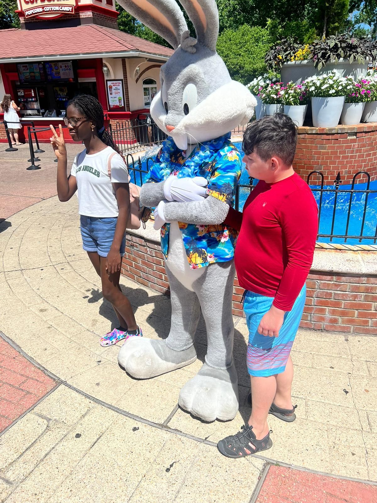 Two people pose with Bugs Bunny wearing a Hawaiian shirt outside a building.