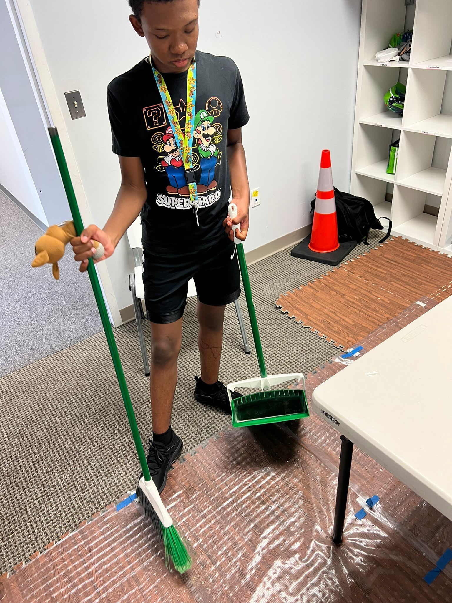 Boy sweeping with a broom in a room with a white table and shelves.