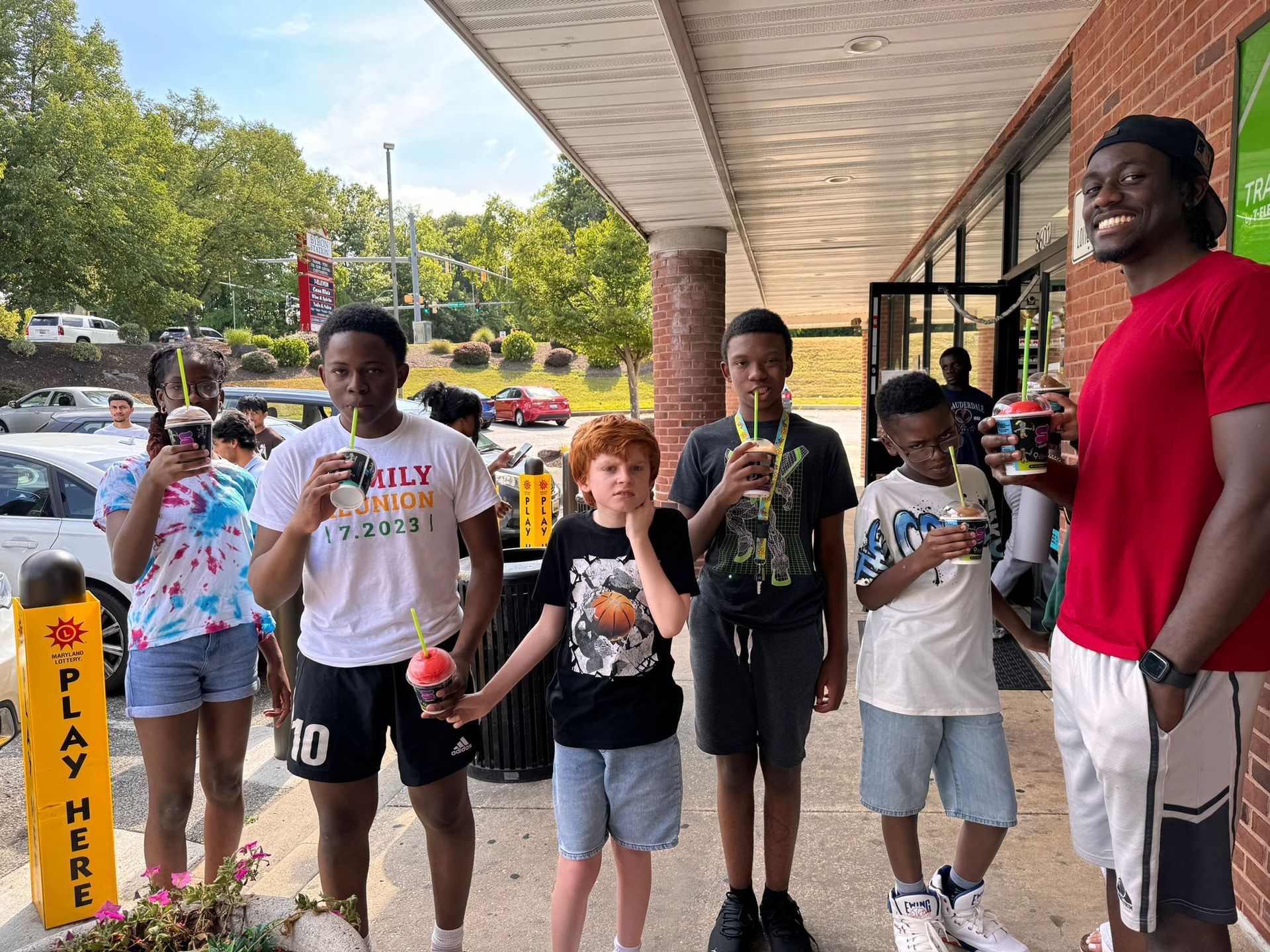 Group of kids and an adult enjoy shaved ice outside a storefront.