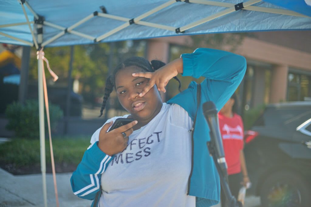 Person making peace signs outdoors under a tent.