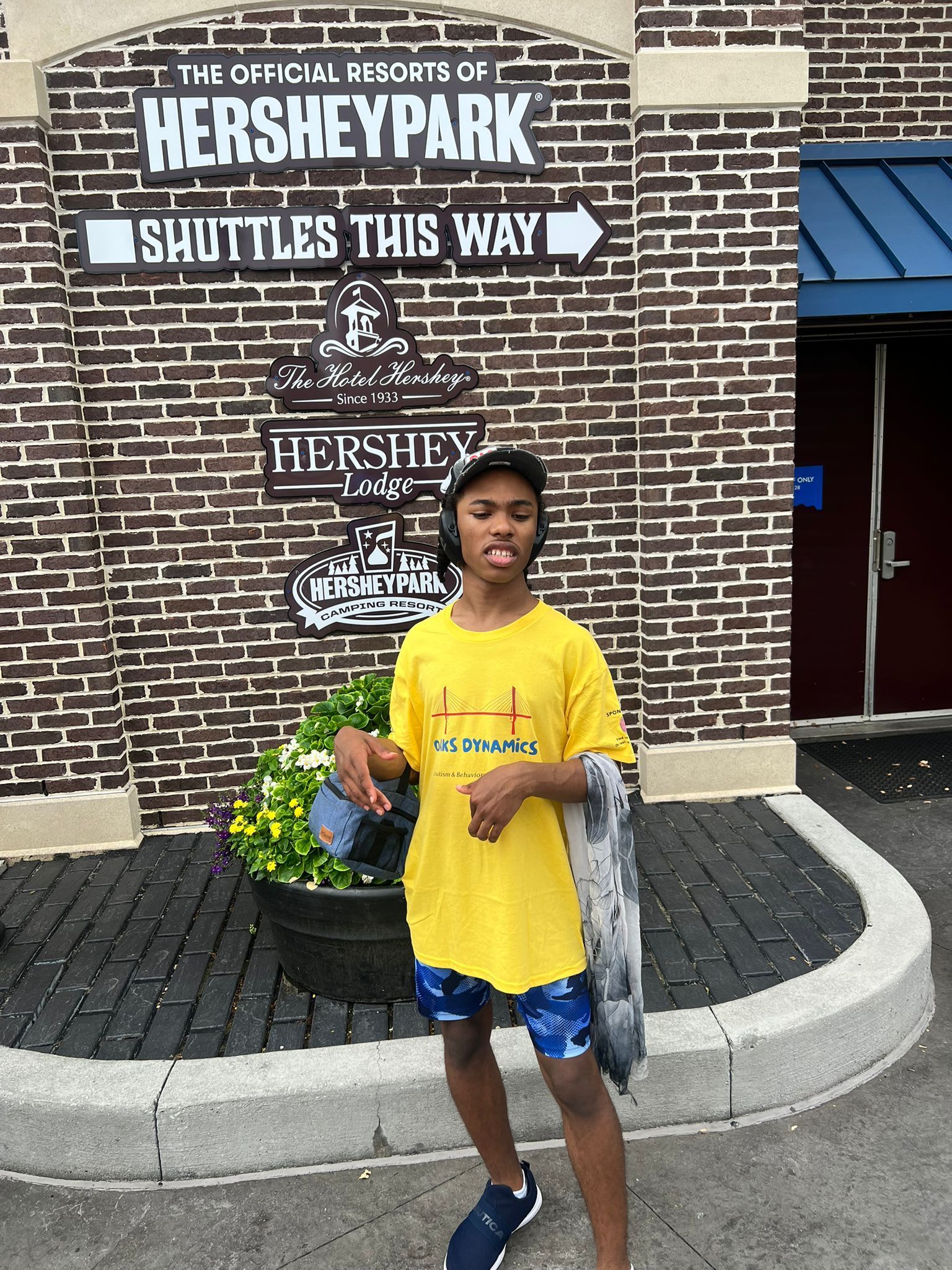 Person in yellow shirt stands in front of Hershey Park sign.