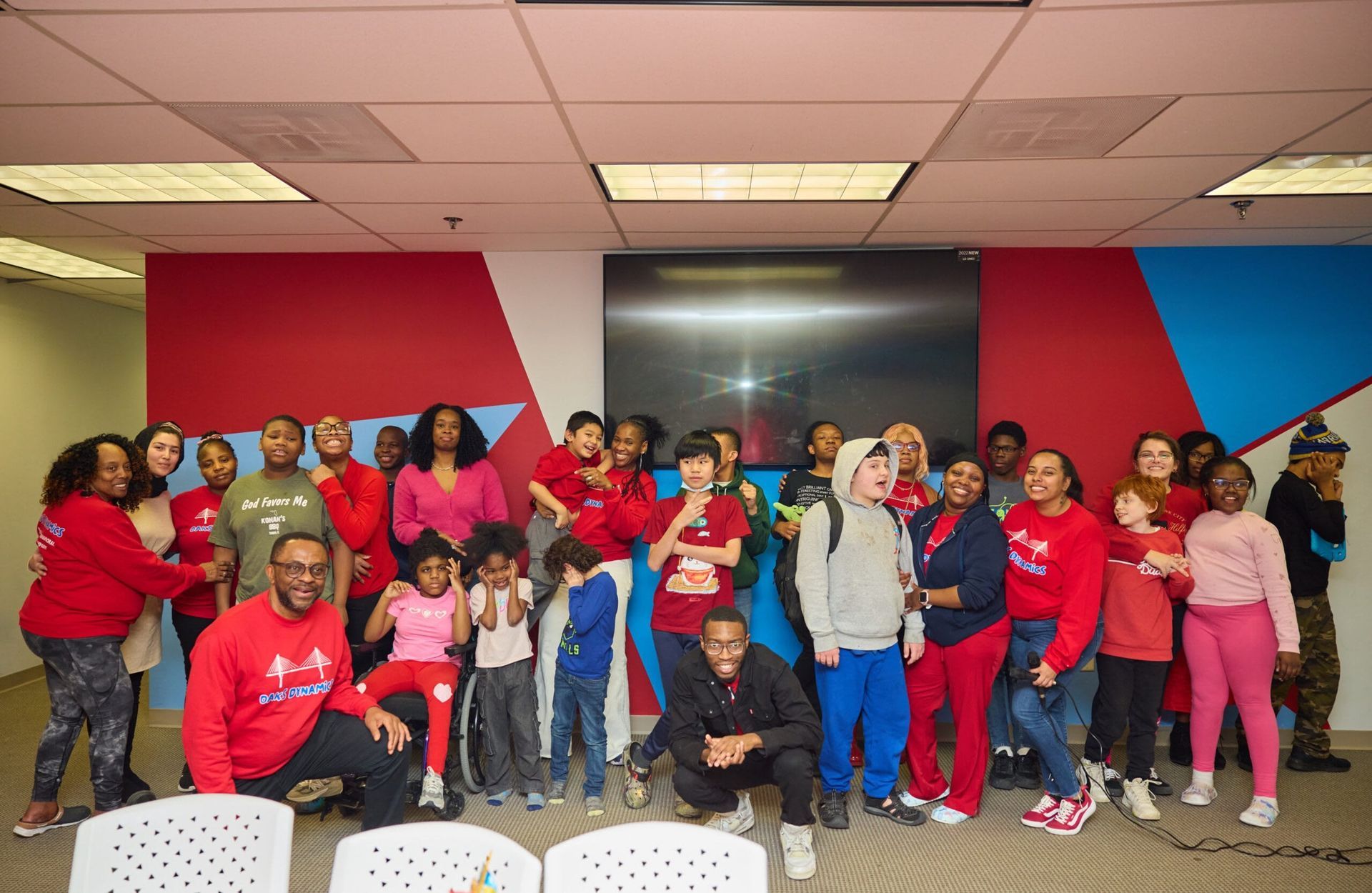 Group of people in red shirts pose in front of a wall with red, blue, and white shapes.