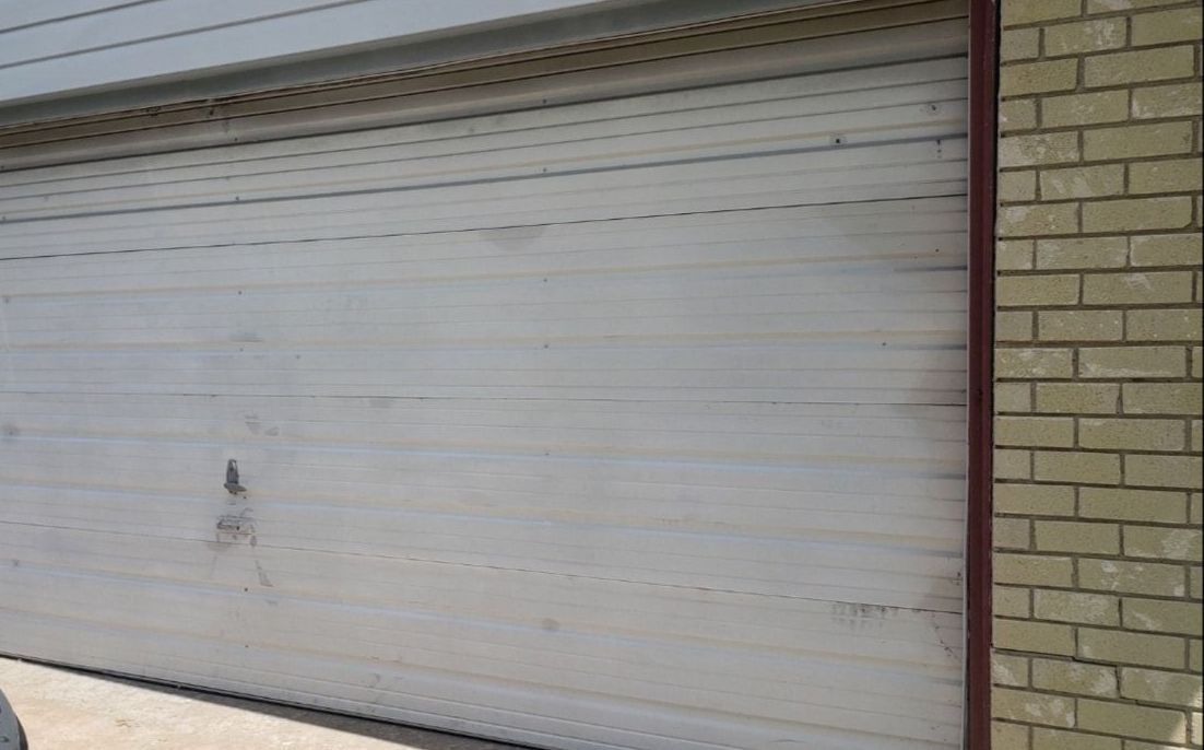 Closed white garage door beside a tan brick wall with a small dark mark near the center