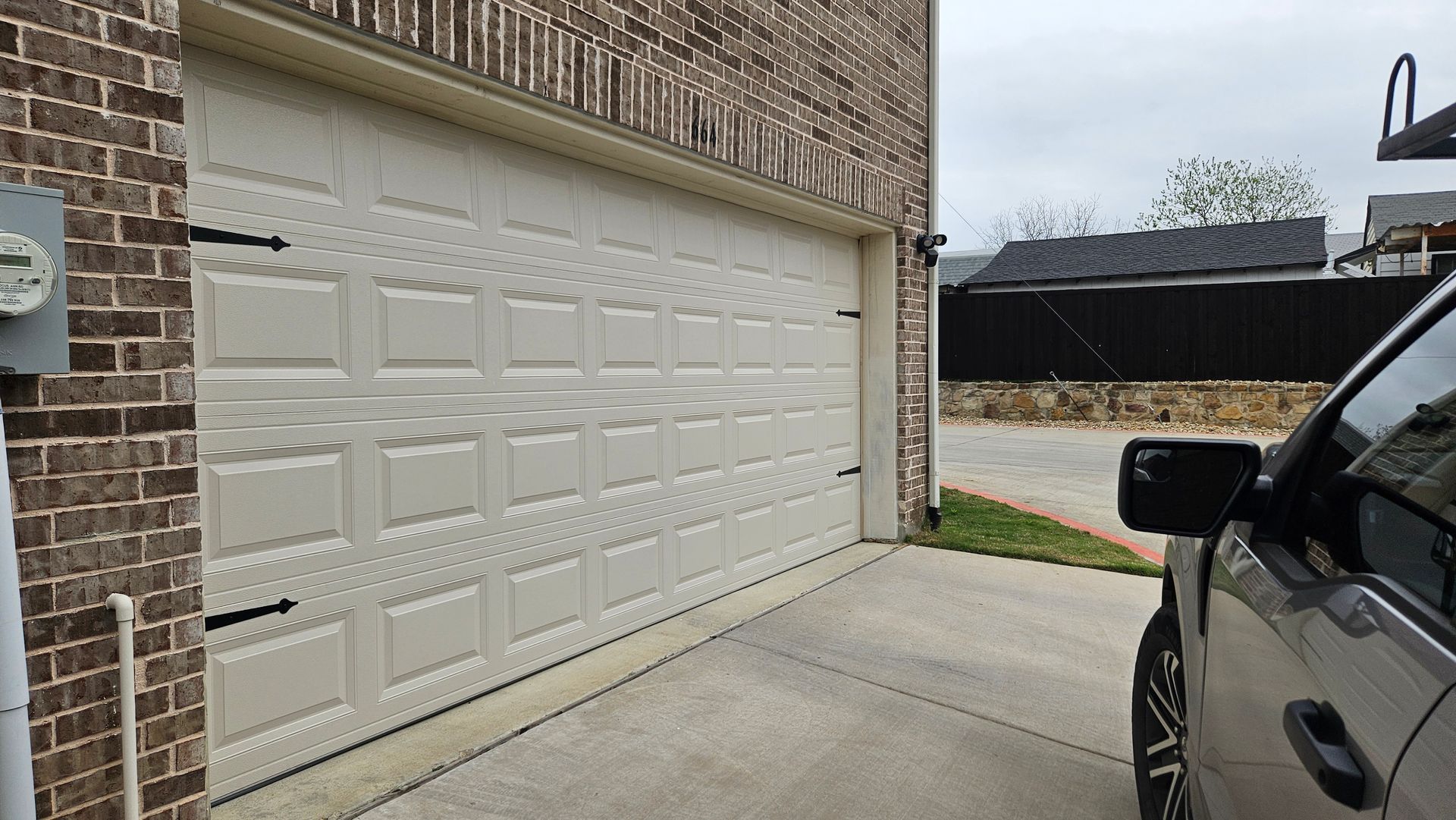 White double garage door on a brick house, with a car parked in the driveway.