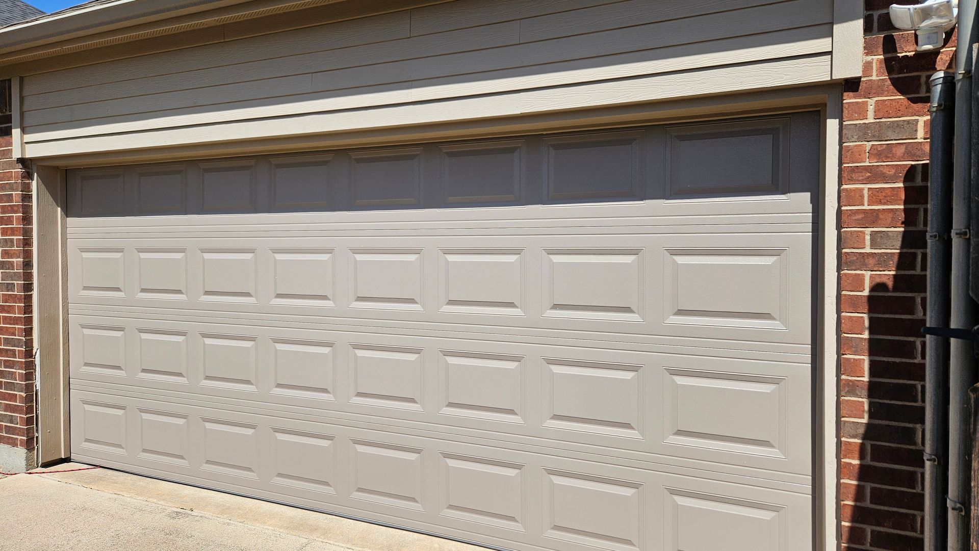 Beige double garage door on a brick house exterior in daylight.