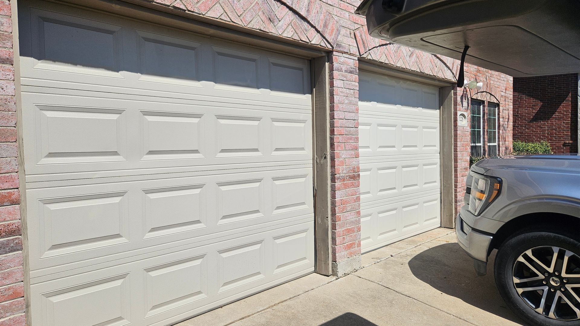 Garage doors beside a brick house driveway, with part of a black SUV parked at right.