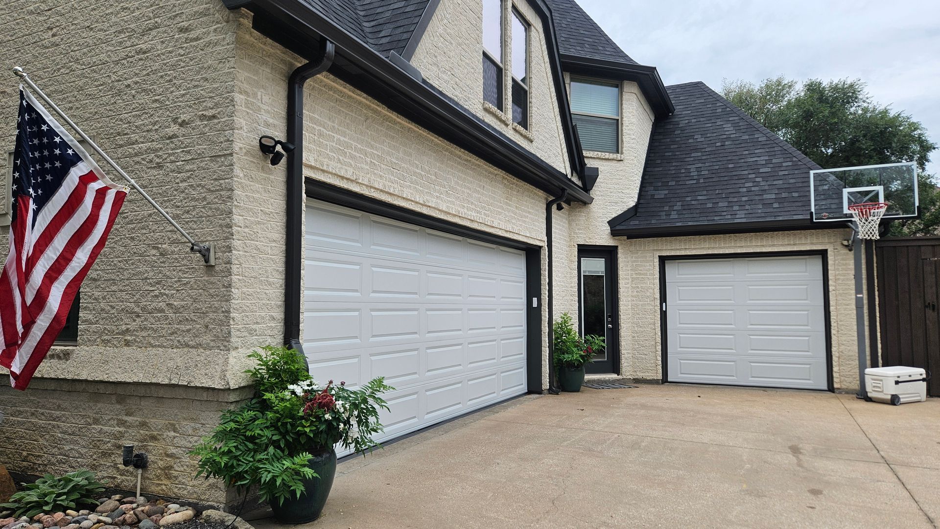 Suburban home exterior with two white garage doors, American flag, and basketball hoop