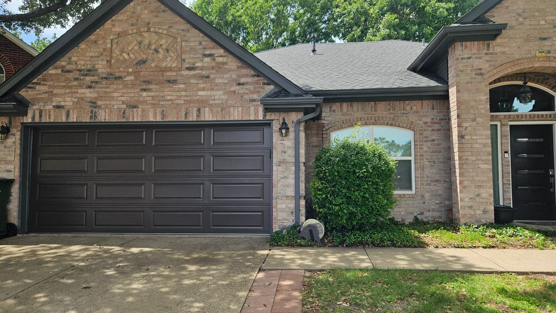 Brick suburban house with dark garage door, front entry, and a small front yard