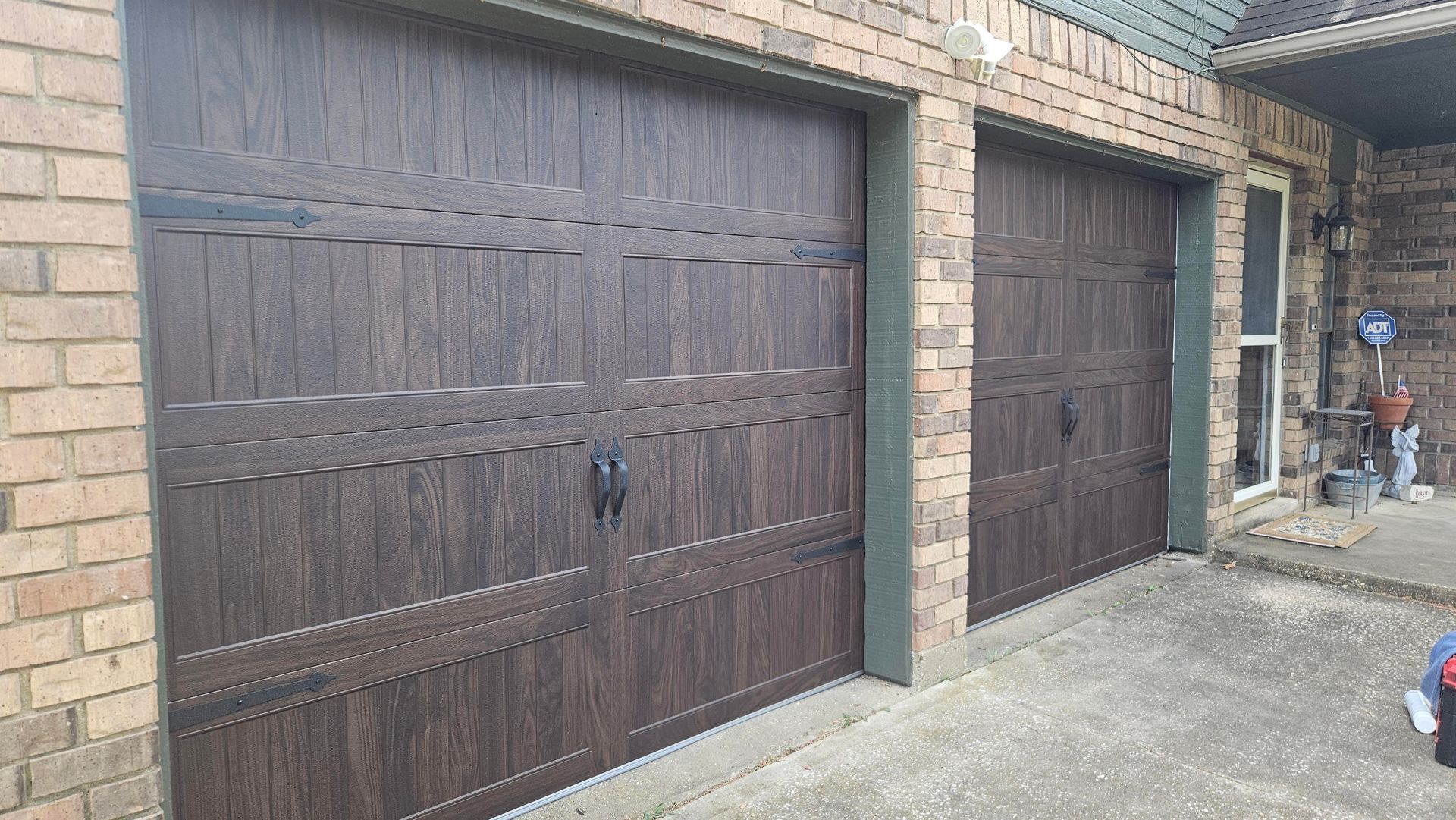 Two brown garage doors on a brick house driveway, with one smaller door beside the larger one.