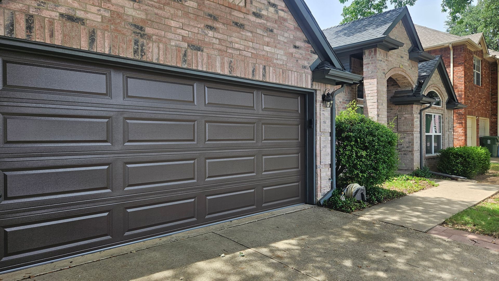 Brown garage doors on a brick house with a driveway and landscaped front entrance