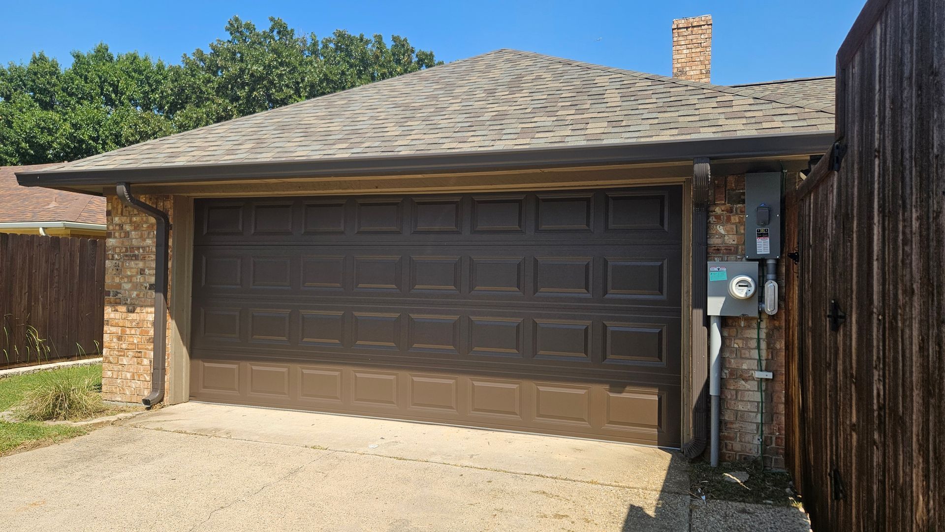 Brown two-car garage on a sunny residential driveway with brick walls and a side utility meter