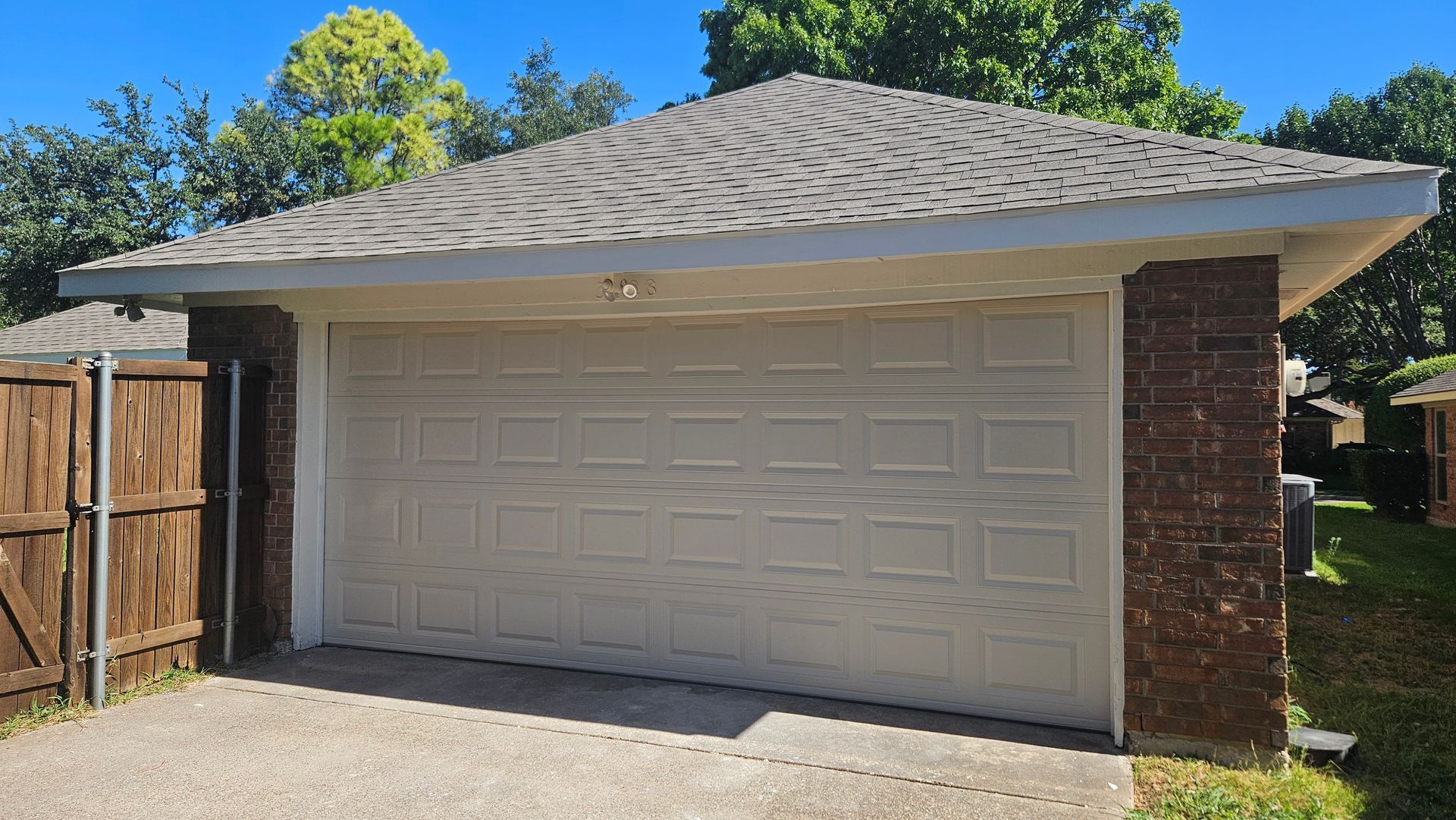 Detached two-car garage with white door, tan trim, and wood fence in a sunny backyard area