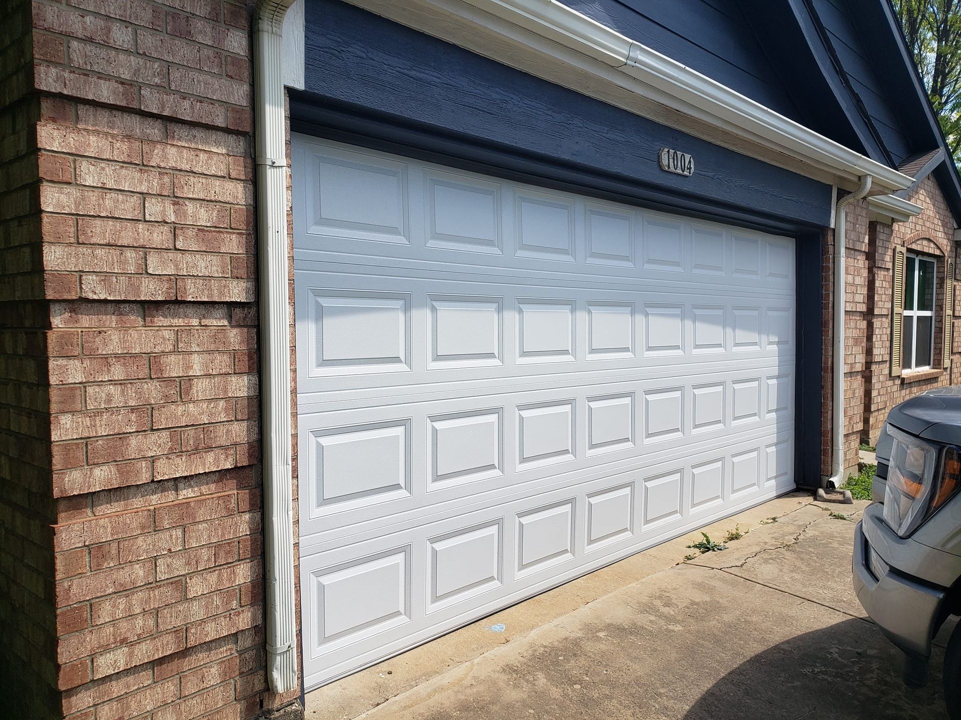 White garage door on a brick house with a driveway and a vehicle partially visible beside it.