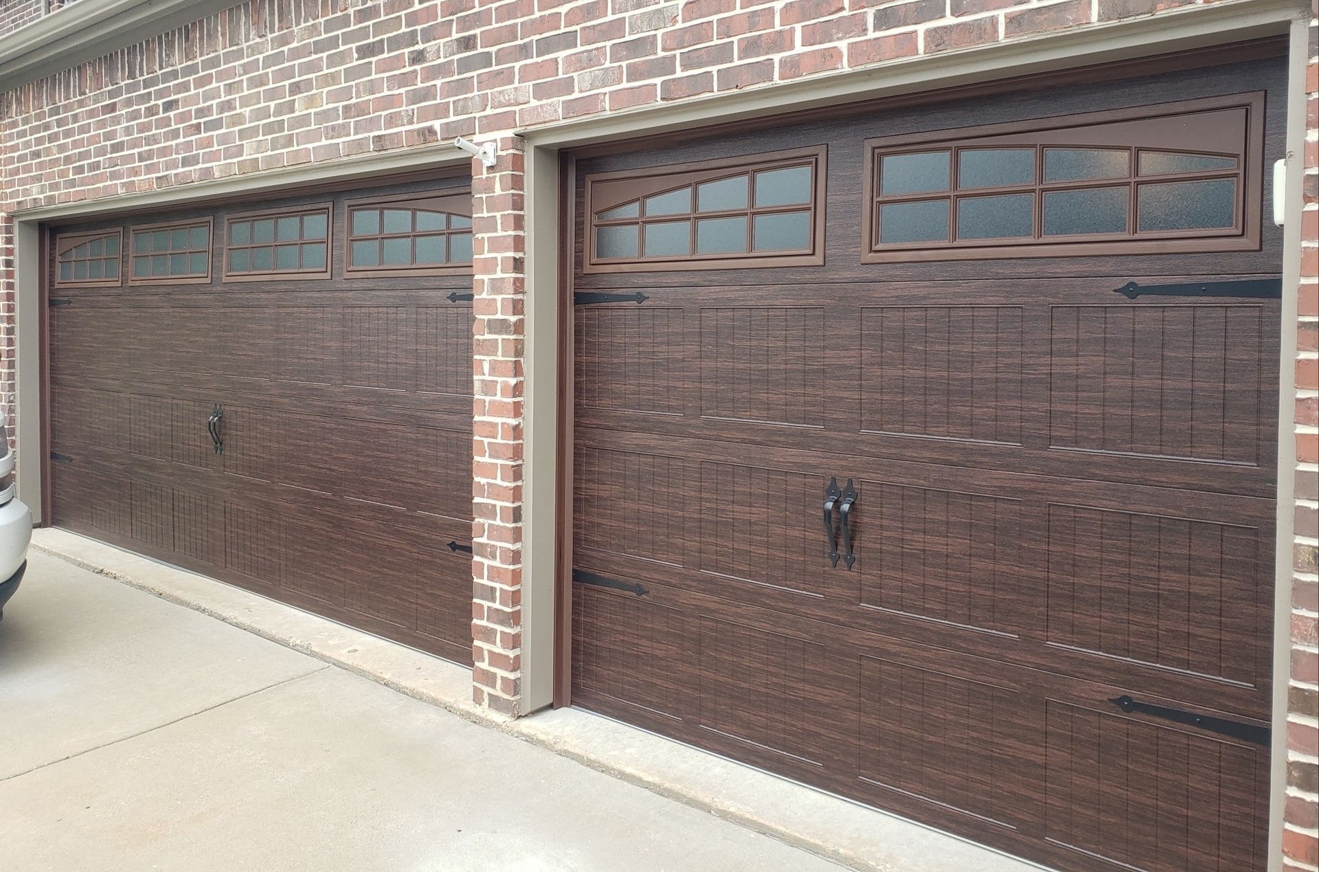 Two brown garage doors with small windows set in a brick house exterior
