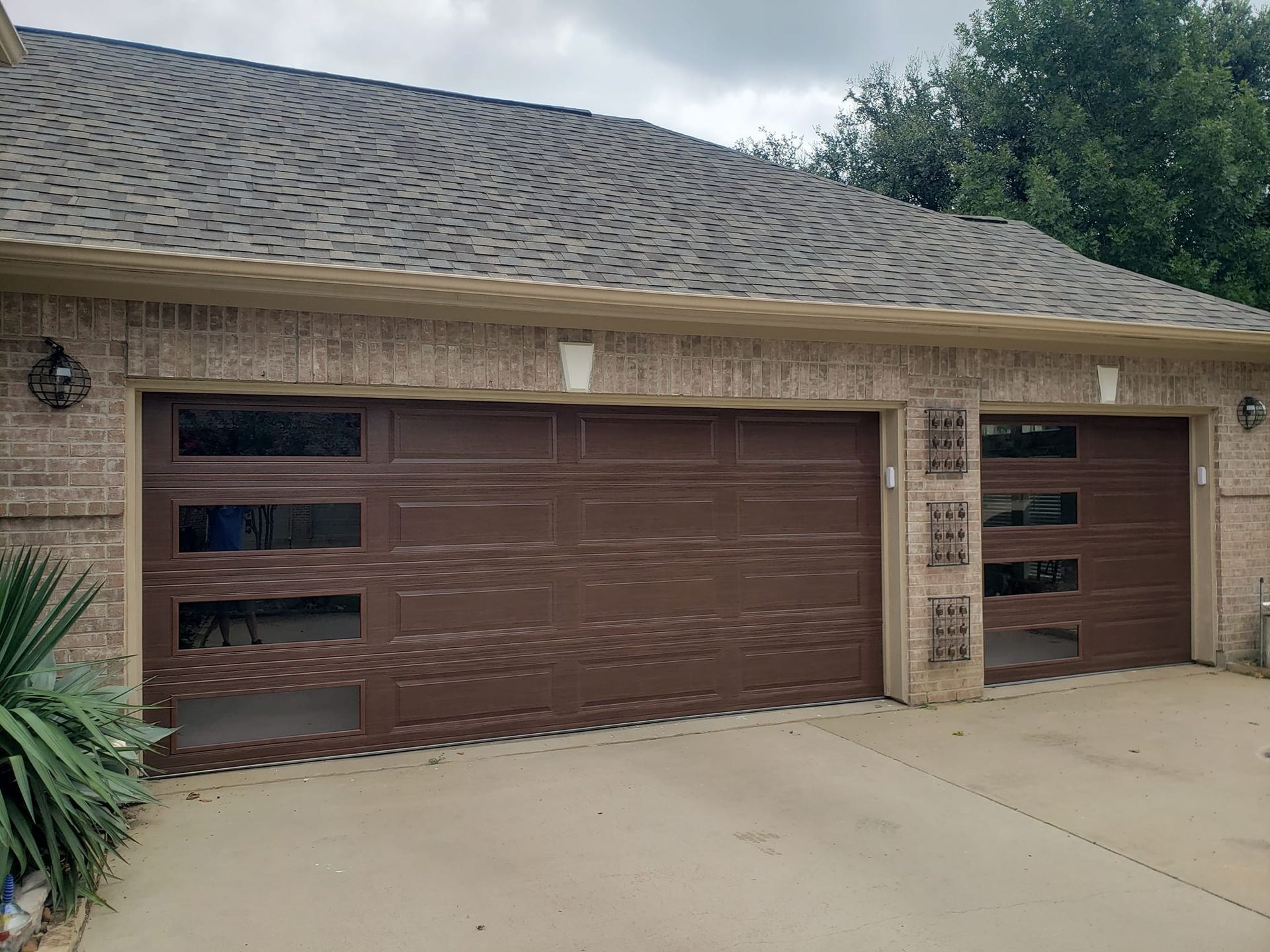 Two brown garage doors on a beige brick house with a concrete driveway