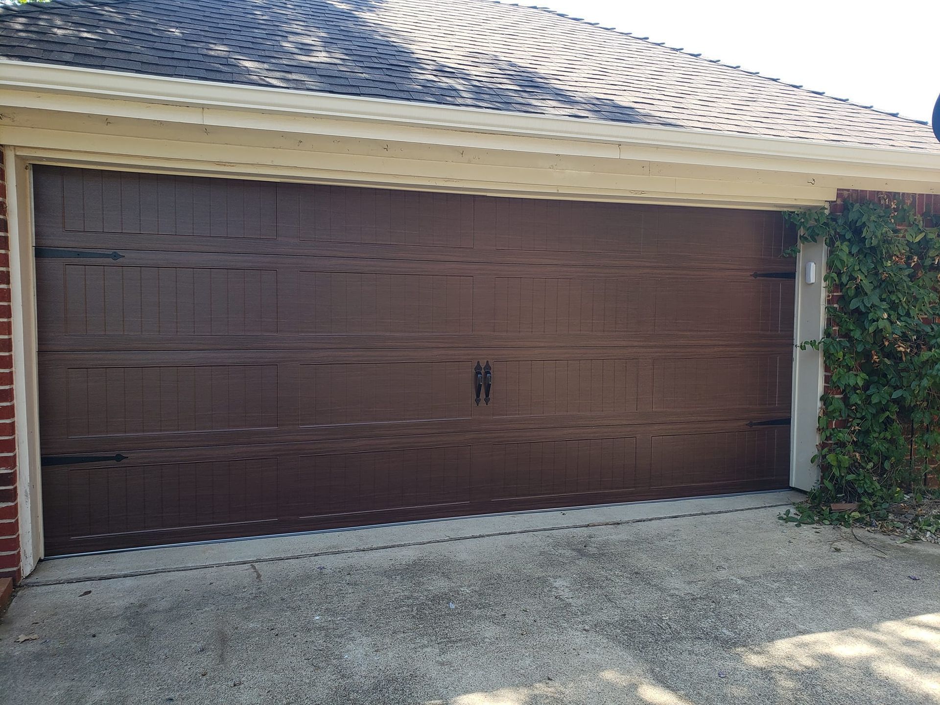 Brown double garage doors on a beige house with gravel driveway and hedges nearby