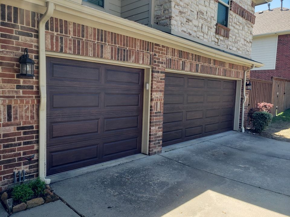 Two brown garage doors on a brick house beside a concrete driveway.