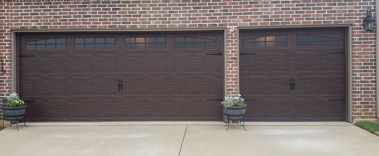 Brick house with two brown garage doors and potted plants on a concrete driveway