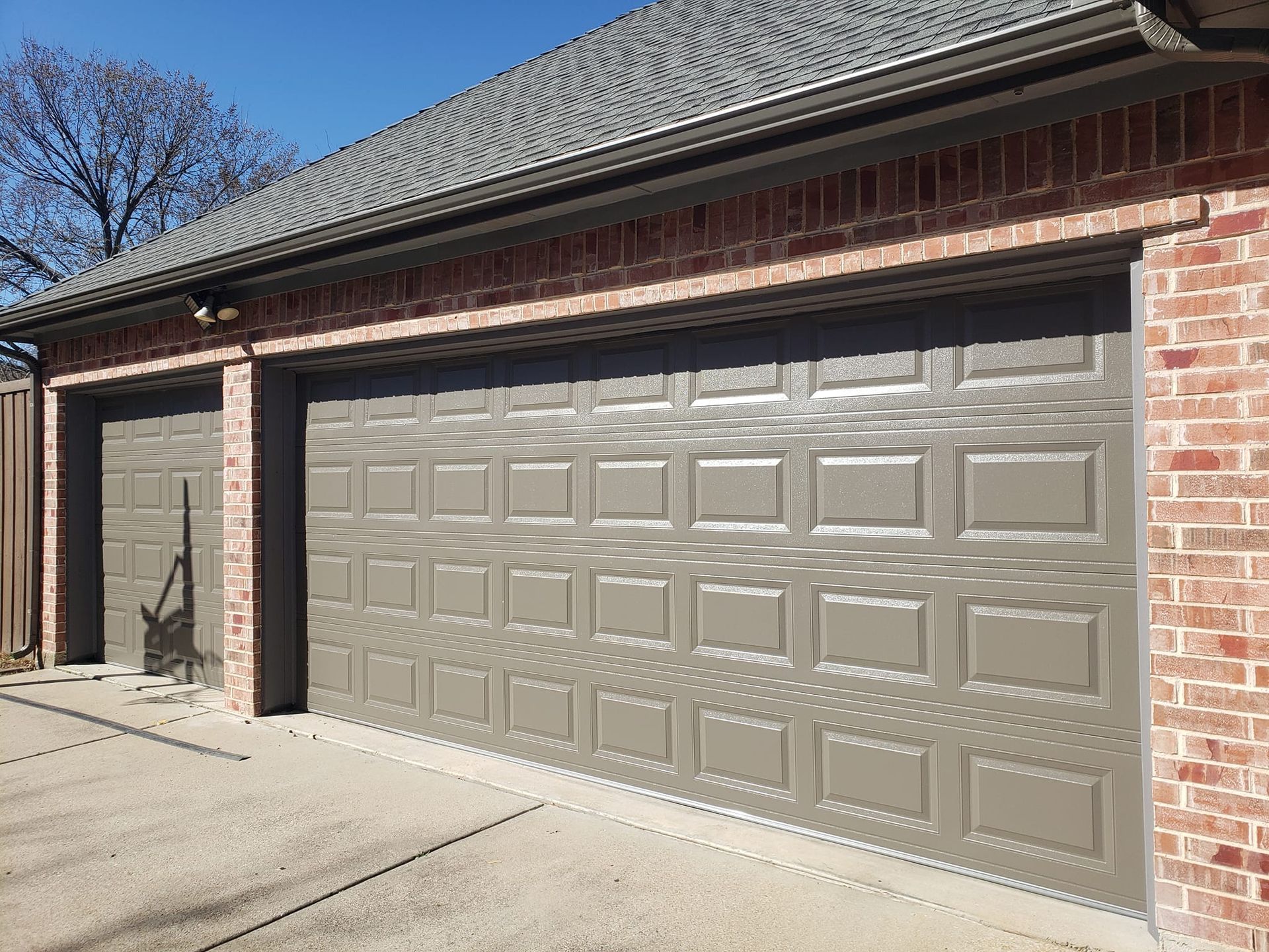 Brick house with two beige garage doors under a shingled roof on a sunny day