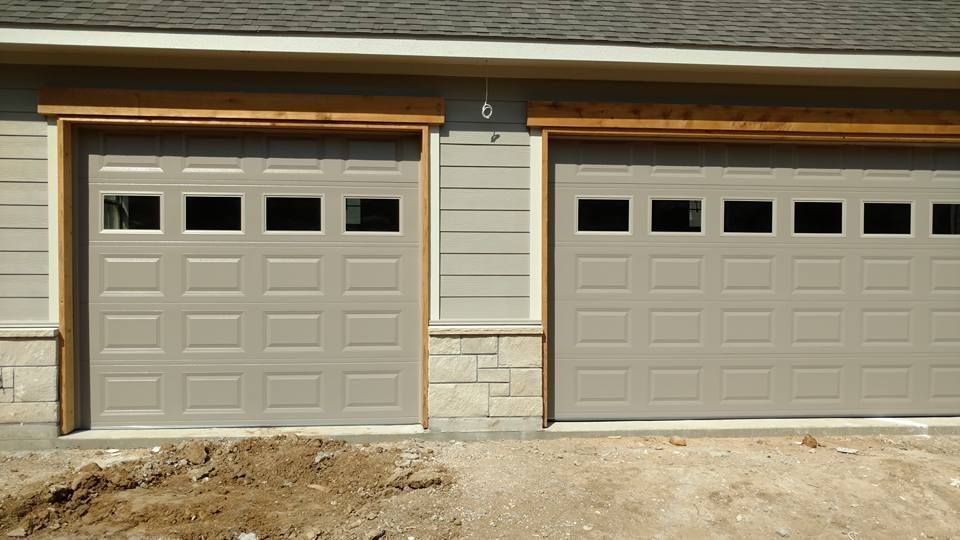 Two beige garage doors on a house exterior with stone and wood trim