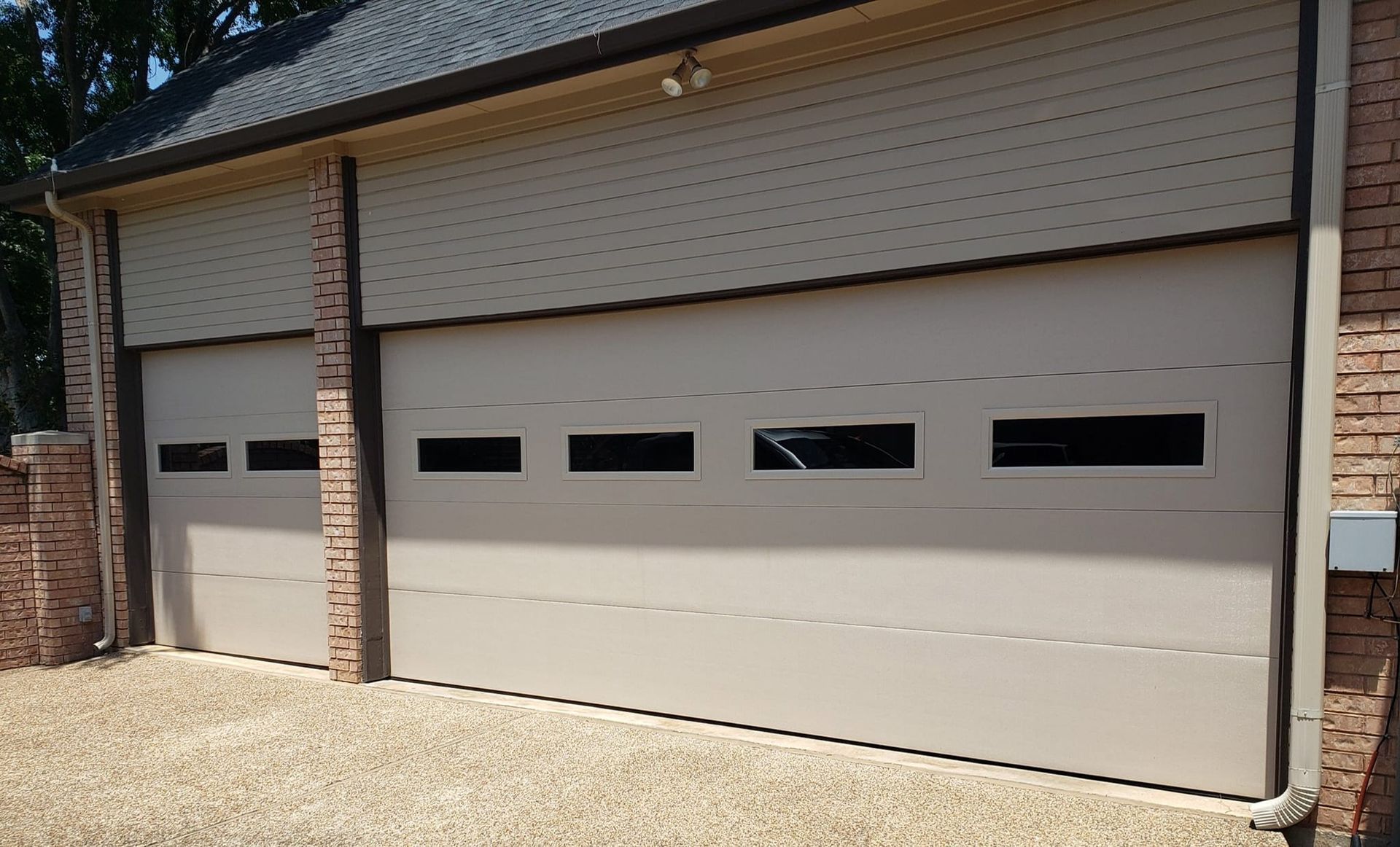 Two cream-colored garage doors on a brick house with small horizontal windows.