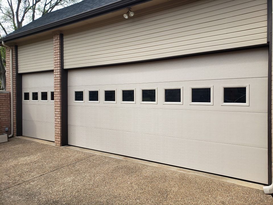 Two beige garage doors with black window panels on a brick house exterior