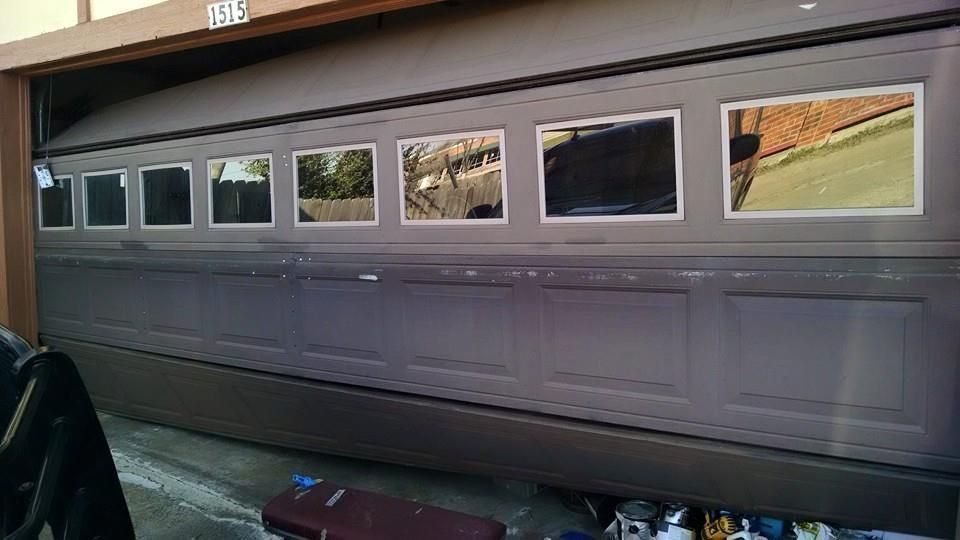 Closed gray garage door with small windows, reflecting a driveway and fence.