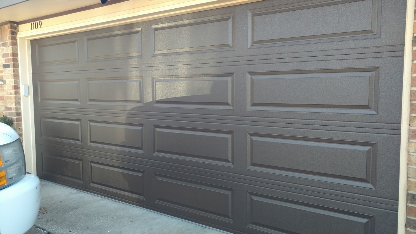 Closed brown garage doors on a house exterior with a driveway beside them.