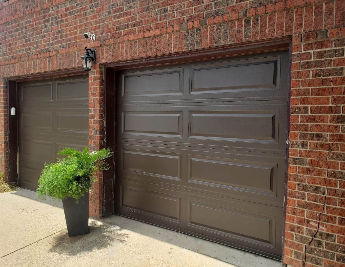 Brick garage exterior with two brown paneled doors and a potted plant by the walkway