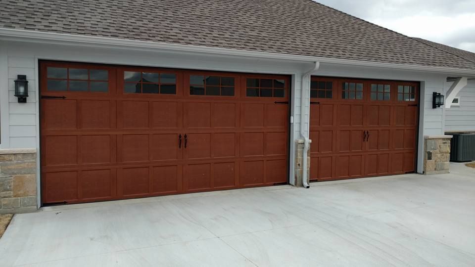 Two red garage doors on a house with a light concrete driveway and stone accents