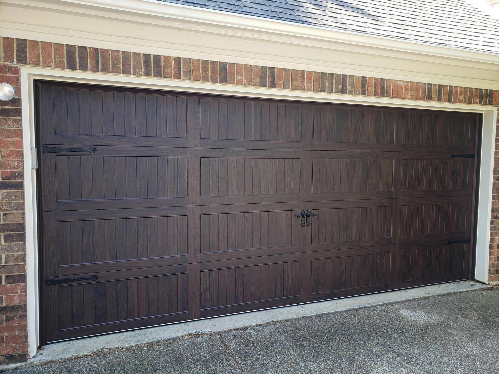 Dark brown garage door set in a brick exterior wall with a light trim and concrete driveway