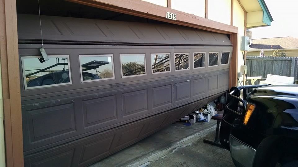 Brown garage door with windows beside a parked black vehicle in a driveway.