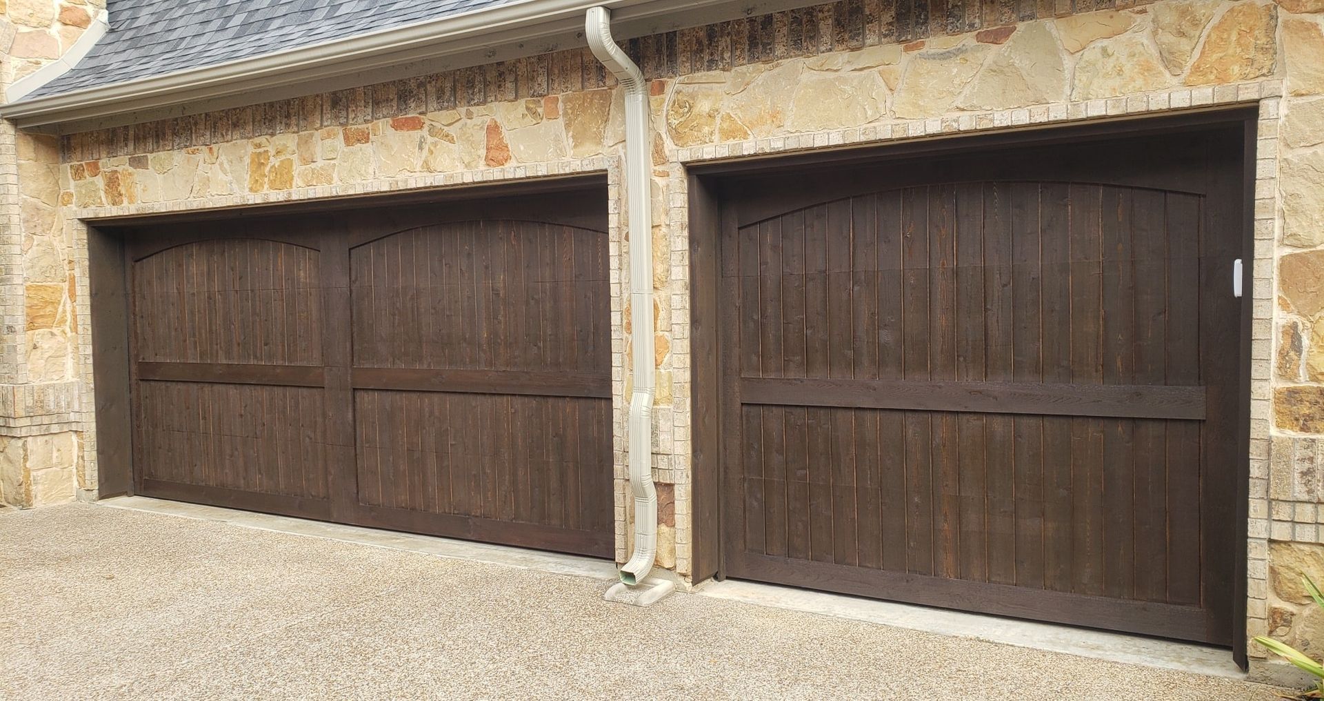 Two dark brown wooden garage doors set in a stone building exterior