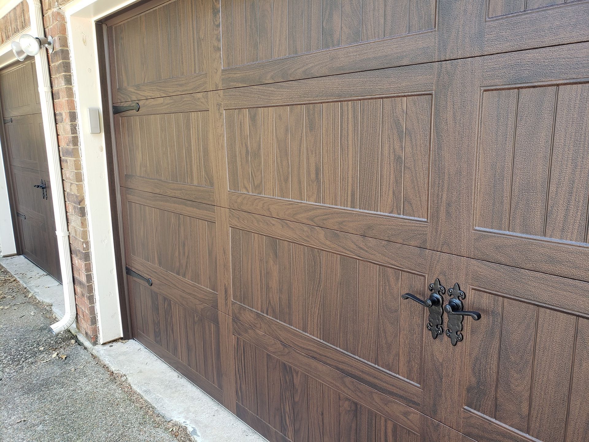 Wooden garage door with decorative panels and black handles beside a stucco wall.